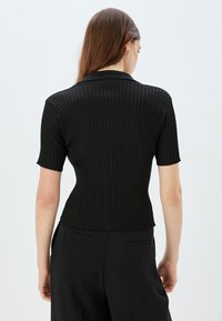 Top negro de manga corta con diseño ajustado, que presenta un collar en punta y una textura suave, visto desde la parte trasera.