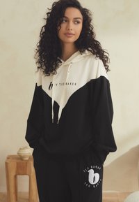 Schwarz-weißes, farblich abgegrenztes Kapuzen-Sweatshirt mit Frontlogo, Kordelzug und übergroßer Passform. Kombiniert mit passenden schwarzen Jogginghosen mit rundem Logo.
