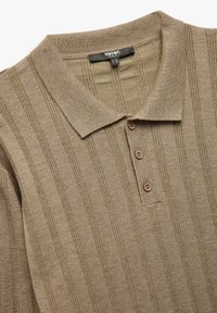 Polo de color beige con textura acanalada vertical, tres botones marrones y un cuello. Fabricado en material ligero, que muestra un diseño limpio.