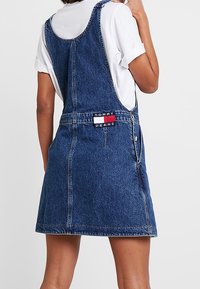 Vestido de mezclilla con tirantes ajustables, un corsé ajustado y una falda acampanada. Presenta un parche con el logo y un cierre de botones en el lateral.