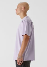 Lys lilla t-skjorte med kort arm og relaxed fit, laget av bomull. Har et ensfarget design og subtile detaljer på ryggen.