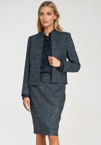 Czarny tweedowy garnitur z dopasowaną marynarką z wysokim kołnierzem i subtelną teksturą, w zestawie z ołówkową spódnicą do kolan.