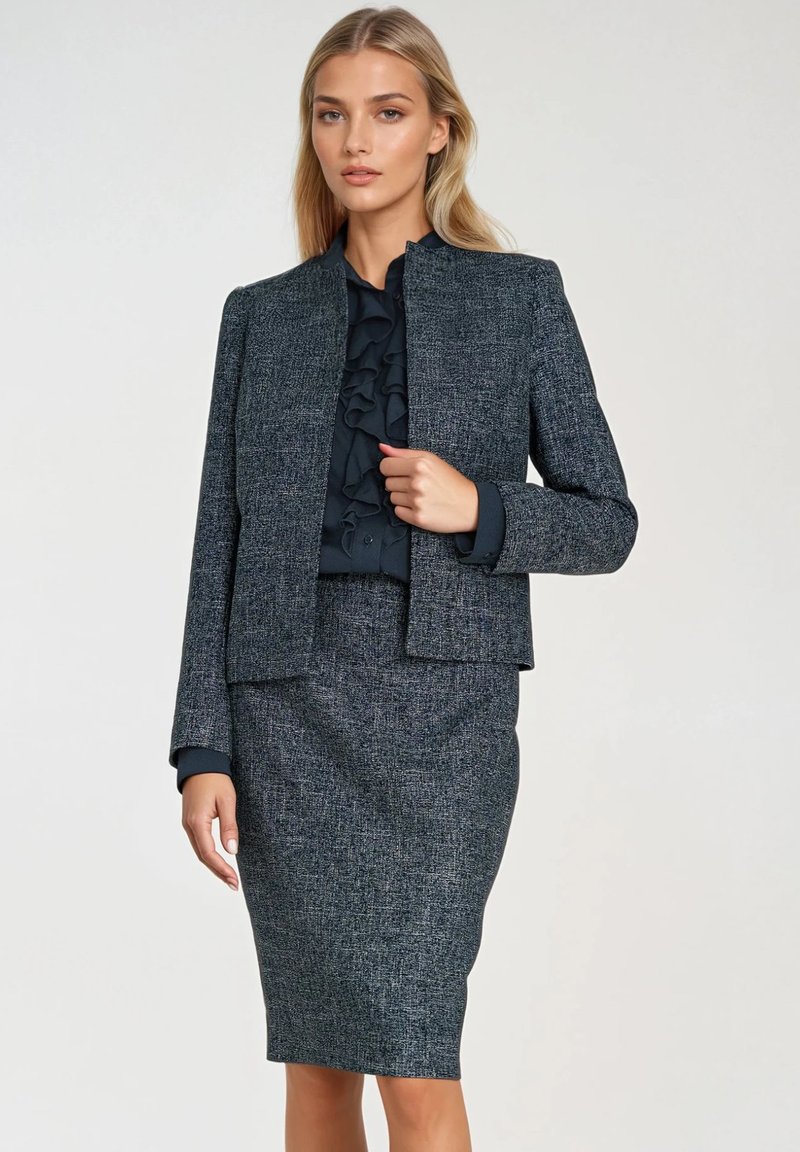 Czarny tweedowy garnitur z dopasowaną marynarką z wysokim kołnierzem i subtelną teksturą, w zestawie z ołówkową spódnicą do kolan.