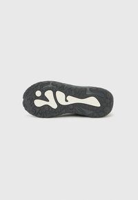 Σόλα μαύρου αθλητικού παπουτσιού με λευκό αφηρημένο σχέδιο, που διαθέτει υφή με σχέδια πέλματος για καλύτερο κράτημα, παρουσιάζεται σε απλό φωτεινό φόντο.