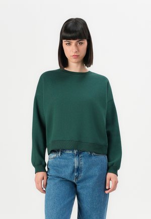 Green cropped sweatshirt with a round neckline, long sleeves, and ribbed cuffs, paired with high-waisted blue jeans. Smooth fabric texture.