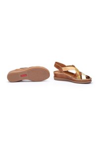 Sandalias de cuña marrón y dorado con correas cruzadas, parte superior de cuero suave, suela de goma texturizada y costuras blancas delgadas a lo largo de los bordes.
