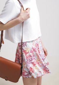 Camisa blanca corta combinada con una falda floral en tonos rosas y pasteles. Bolso cruzado de cuero marrón con correa larga y un sutil detalle de herrajes.