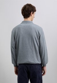 Polo gris à manches longues avec col, texture douce et coupe décontractée, associé à un pantalon en velours côtelé foncé, vu de dos.