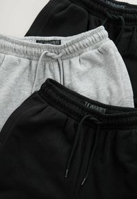 Drei Paare von lässigen Jogginghosen in Schwarz, Grau und einem weiteren dunklen Farbton. Jedes Paar verfügt über einen elastischen Bund und verstellbare Kordeln.