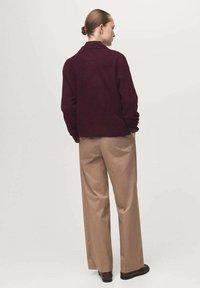 Maglione in lana bordeaux con una vestibilità comoda, abbinato a pantaloni beige con gamba larga. Texture liscia e design minimale.