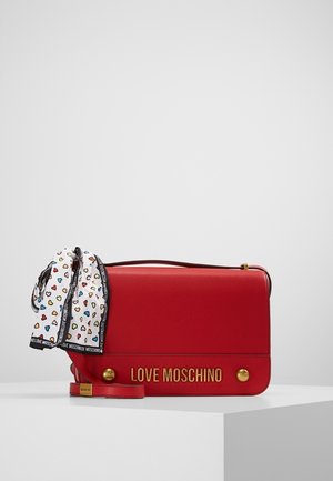 Czerwona torebka Love Moschino ze złotymi okuciami oraz biała apaszka ozdobiona kolorowymi wzorami serc, zawiązana na uchwycie.