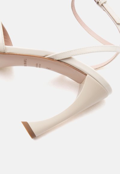 Εκρού ψηλοτάκουνο σανδάλι με λεπτά λουράκια και φουσκωμένο τακούνι, απεικονισμένο από κοντινή πλευρική γωνία σε λευκό φόντο.