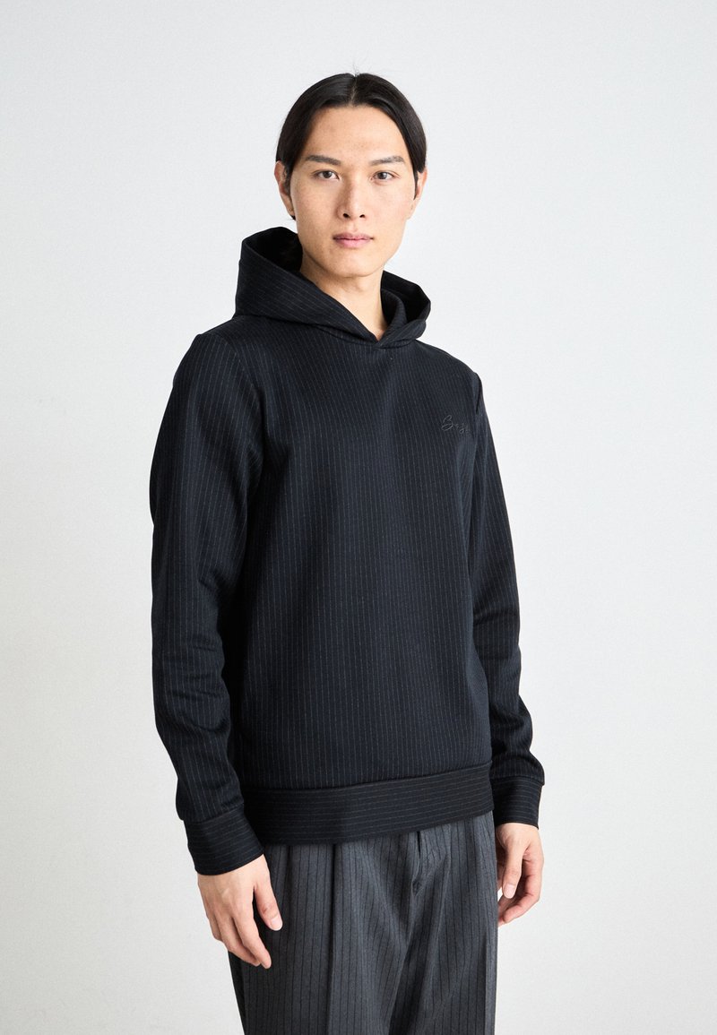 Sweatshirt à capuche noir en tissu texturé avec des rayures verticales. Il comporte une poche kangourou à l'avant et des poignets et un ourlet côtelés.
