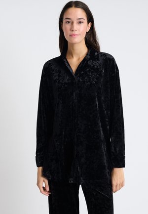 Camisa de terciopelo negro con cuello y mangas largas, que presenta una textura suave y un corte holgado.