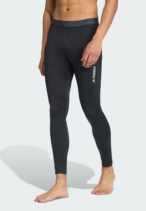 Schwarze, enganliegende Leggings aus dehnbarem Stoff mit einem breiten Bund und einer Seitentasche, die ein weißes Logo auf dem Oberschenkel trägt.