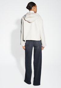 Felpa grigia chiara con cappuccio, con spalle ribassate e maniche lunghe, abbinata a jeans larghi in denim scuro.