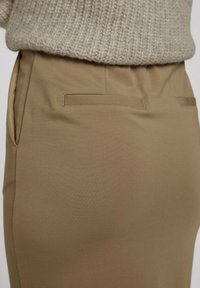 Jupe crayon kaki en tissu lisse, dotée de poches latérales et d'une coupe ajustée avec des éléments de design minimalistes.