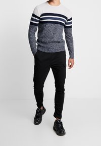 Navy and white striped knit sweater with a textured design, paired with black cargo pants and black athletic shoes.