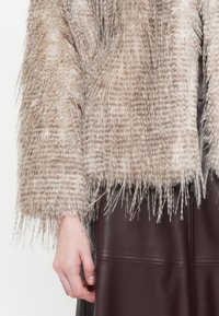 Faux fur cropped jacket in tan with textured, long fringes. Accompanied by a dark burgundy leather skirt with visible seam accents.