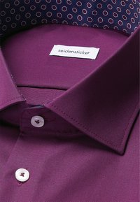 Lila Hemd aus glattem Stoff mit kontrastierender Krageninnenseite mit einem kreisförmigen Muster und weißen Knöpfen.