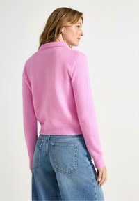 Rosa ylletröja med ribbat krage och muddar, kort design och mjuk textur. Matchas med ljusblå jeans med hög midja.