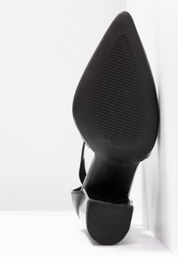 Chaussure à talon haut noire avec un bout pointu, finition brillante et semelle texturée. Présente un design de talon épuré et des accents minimalistes.