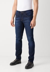 Mörkblå denimjeans med två framfickor, ljus sömnad och rak passform. Bärs med en enkel vit linne och svarta skor.