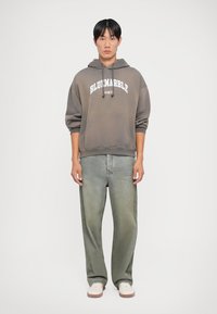 Sweatshirt cinza com capuz e texto "BLUIMARBLE", emparelhado com jeans de perna larga verde-claro e ténis brancos. Ajuste casual e relaxado.