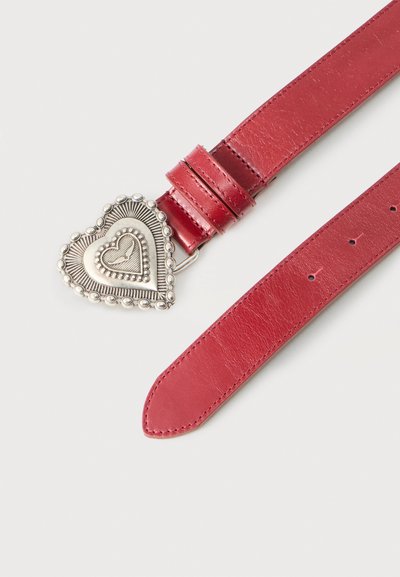 Κόκκινη δερμάτινη ζώνη με ασημένια αγκράφα σε σχήμα καρδιάς, διακοσμημένη με ανάγλυφα σχέδια και μικρές στρογγυλές καρφίτσες.