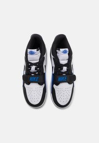 Svarta och vita sneakers med blå detaljer, med en perforerad tå, platta skosnören och ett sidoband med "NIKE"-logotyp.