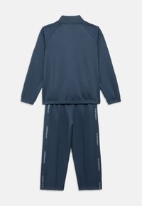 Trening bleumarin cu jachetă cu fermoar și pantaloni cu talie elastică. Prezintă mâneci și pantaloni cu margini striate și brandul vertical „JORDAN” pe părți. Textură netedă.