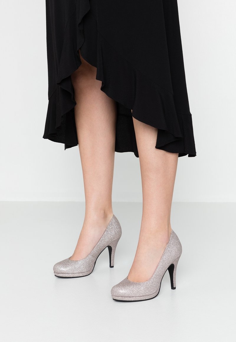 Tacones altos plateados brillantes con punta redondeada y delgado tacón de aguja negro, con un acabado liso de purpurina y silueta curvada.