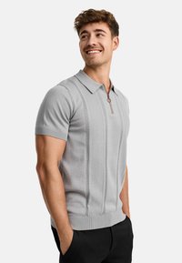 Light gray short-sleeve polo shirt with a zippered collar, textured vertical stripes, and ribbed edges. Worn with black pants.