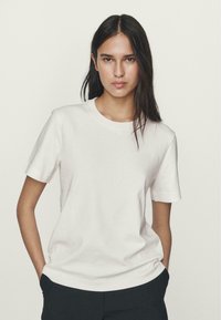 T-shirt bianco a maniche corte realizzato in materiale morbido, con scollatura rotonda e vestibilità rilassata, caratterizzato da una texture liscia.