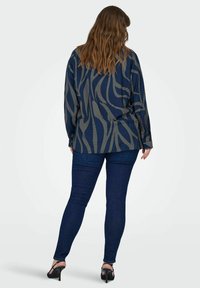 Mornarska bluza s valovitim uzorkom u bež boji, dugih rukava, opuštenog kroja. Uparena s tamnoplavim skinny trapericama i crnim sandalama na visoku petu.