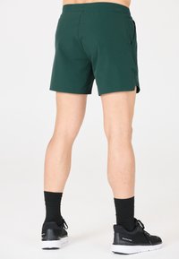Grüne Sportshorts mit glatter Textur, seitlichen Taschen und einem leicht taillierten Schnitt, kombiniert mit schwarzen Schuhen und Socken.
