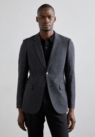 Tmavě šedý přizpůsobený blazer s klopami a dvěma předními kapsami. Nositelný přes černé polo tričko, které má hladkou, strukturovanou texturu.