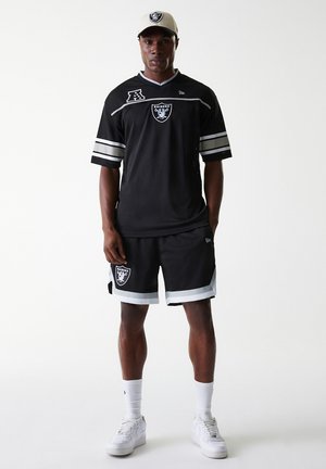 Black mesh jersey with white and silver stripes, featuring Raiders logo. Paired with black shorts and white sneakers. Cap in light color.