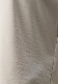 Tissu beige clair avec une texture lisse et un éclat subtil, présentant des lignes douces et ondulées ainsi qu'une légère chute. Pas de motifs ou d'accents notables.