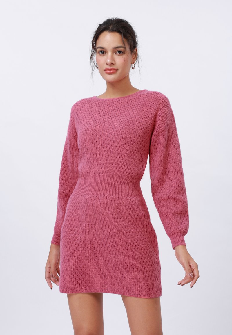 Rosa strikket kjole med et teksturert mønster, lange ballongsleeves og en tilpasset midje. Stoffet ser mykt og litt elastisk ut.