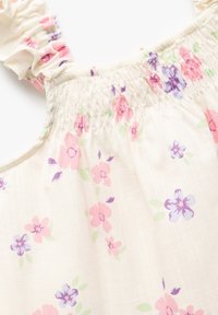 Hvidt stof med et blomsterprint, der har pink og lilla blomster. Rynkede stropper og indsamlet smock ved halsudskæringen. Blød tekstur.