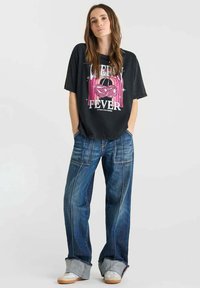 Camiseta gráfica negra con diseño "Cherry Fever", combinada con jeans de mezclilla azul de pierna ancha con costuras en contraste y dobladillos sin terminar, zapatillas blancas.