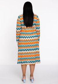 Ein gemustertes knielanges Kleid mit Zickzackstreifen in Orange, Türkis und Schwarz. Lange Ärmel und runder Ausschnitt; glattes, strukturiertes Gewebe.