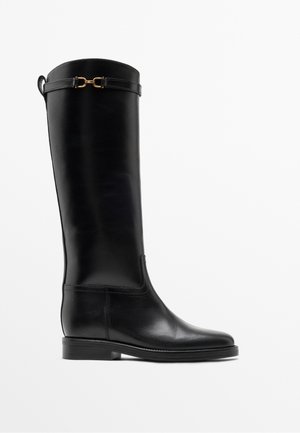 Botte haute en cuir noir avec un petit talon et un détail de boucle dorée près du haut, montrée de profil sur fond blanc.