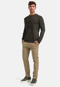 Maglione lavorato a maglia verde scuro con righe testurizzate, abbinato a pantaloni chinos beige e sneaker grigie. Outfit casual con una vestibilità rilassata.