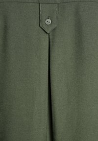 Tkanina w oliwkowym kolorze z centralnym pionowym fałdem i jednym pasującym guzikiem przyszytym na przyszytej zakładce nad fałdem.