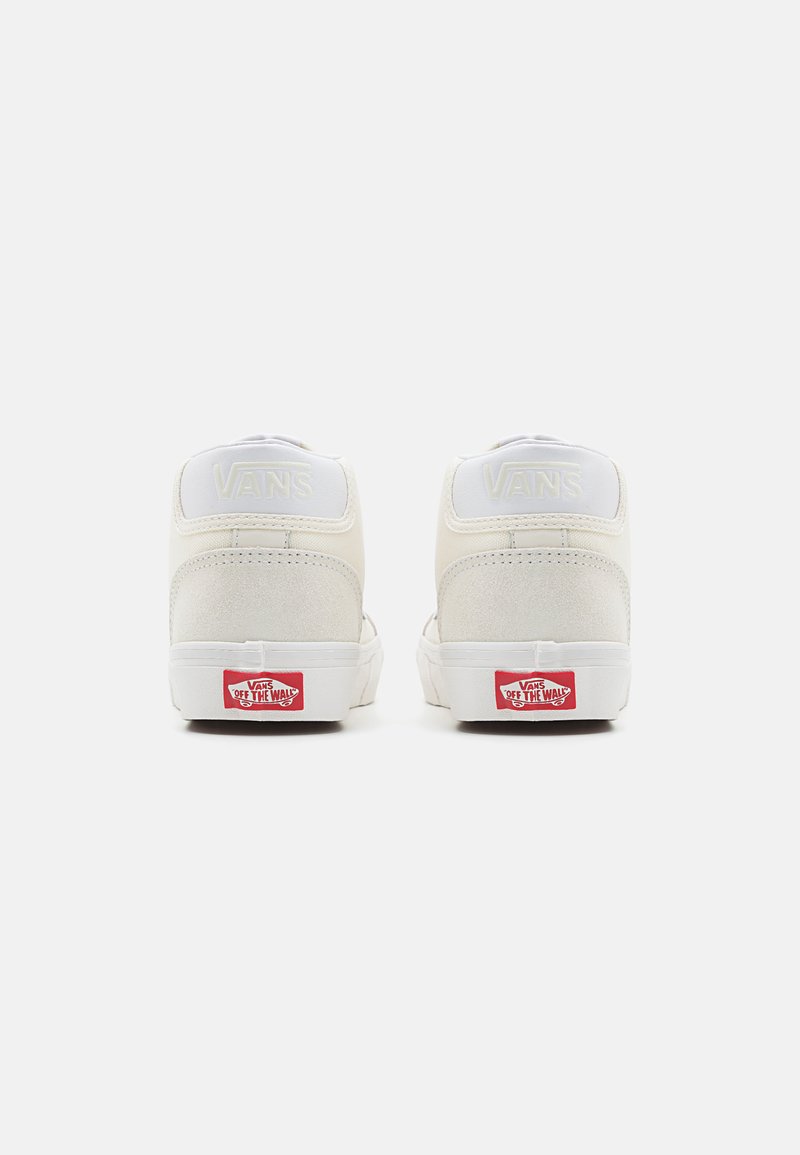 Baskets Vans crème avec un design montante. Matériaux en daim et toile doux, accents blancs et logo rouge sur le talon. Texture lisse.