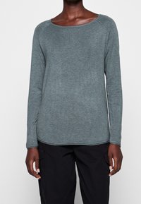 Pitkähihainen paita pehmeässä, tumman teal-värisessä kankaassa, jossa on leveä kaula-aukko, raglan-hihat ja hieman kaareva helma. Ei näkyviä kuvioita tai yksityiskohtia.