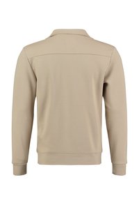 Suéter beige de manga larga, con cuello tipo polo, tejido texturizado y dobladillo recto. Presenta un respaldo liso y un detalle minimalista.