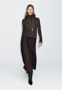 Brown turtleneck sweater paired with a dark brown maxi skirt and black pointed-toe ankle boots. Simple silver necklace accentuates the look.
